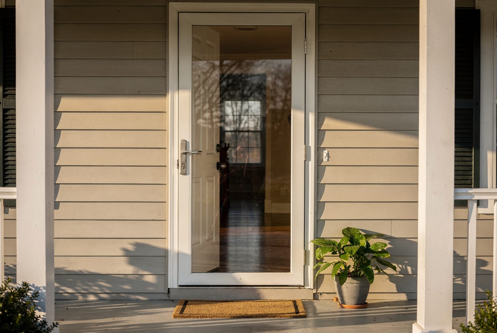A full-view glass storm door on the front of a tidy NC home, the main entry door open behind it letting warm daylight into the hall, screen visible, real light on the porch.