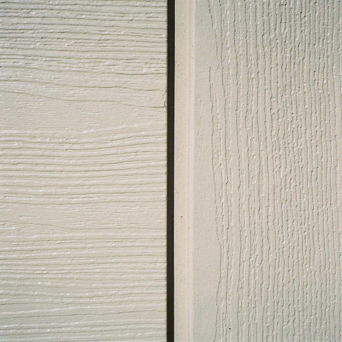 Close-up texture pair: a vinyl siding surface with its lighter, subtly molded grain beside a fiber-cement board with a denser, deep embossed wood-grain texture.