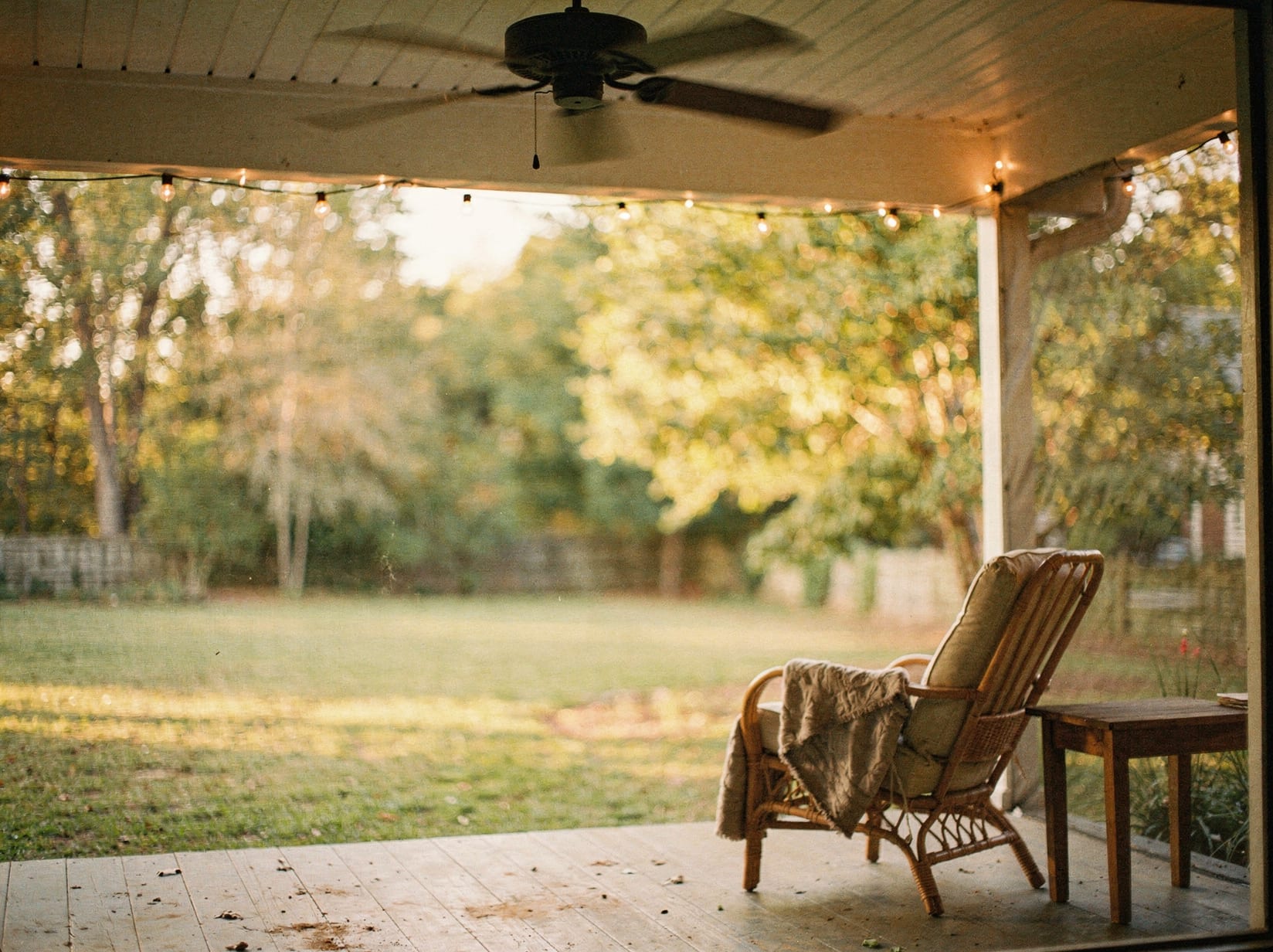A modest, genuinely appealing screened porch on a North Carolina home in warm evening light, with a ceiling fan and comfortable chairs.