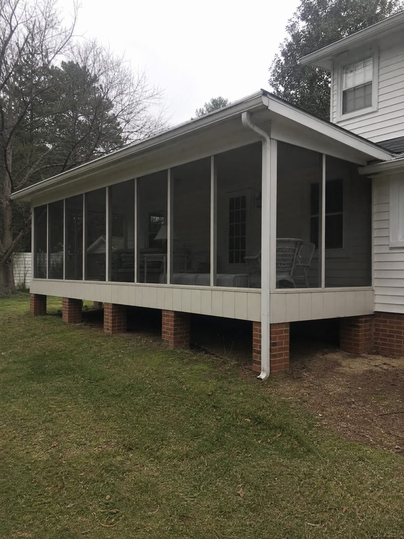 An existing screened-in back porch standing on an open brick pier foundation, the gap beneath the porch floor visible between the piers.