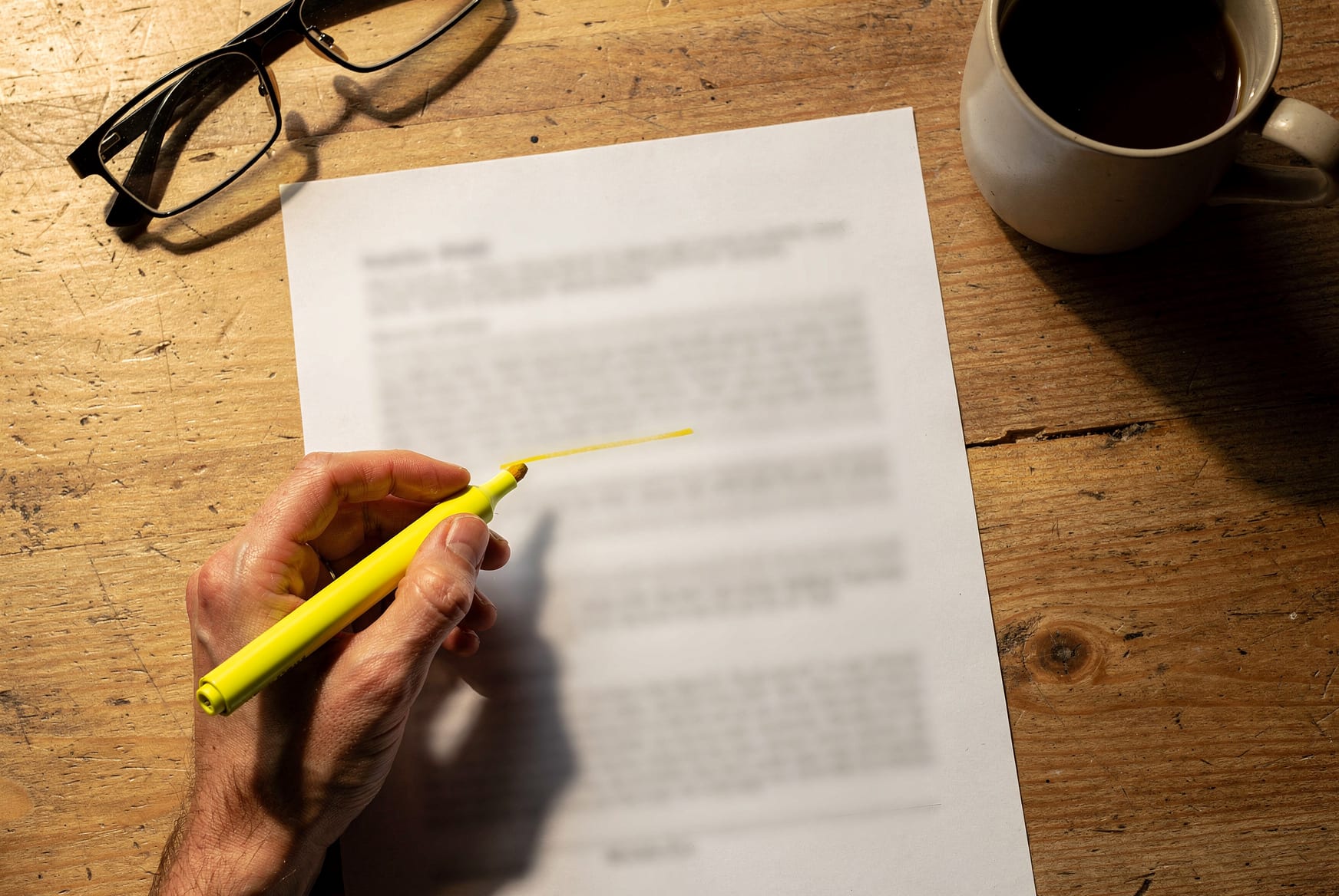Overhead view of a hand circling a line on a printed window quote with a pen, a highlighter resting across another line, reading glasses and coffee at the edge of the table — reading the line items on your own clock.