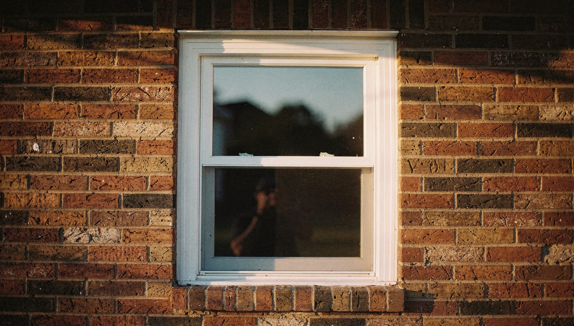 A clean white vinyl double-hung replacement window set in a red-brick North Carolina home exterior in warm afternoon daylight.