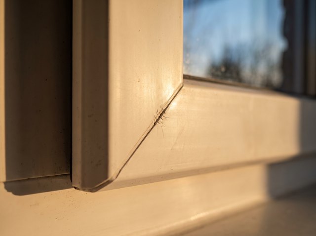 Macro of a white vinyl window frame corner joined mechanically — a visible thin seam line where the two mitred frame pieces meet rather than a fused joint.