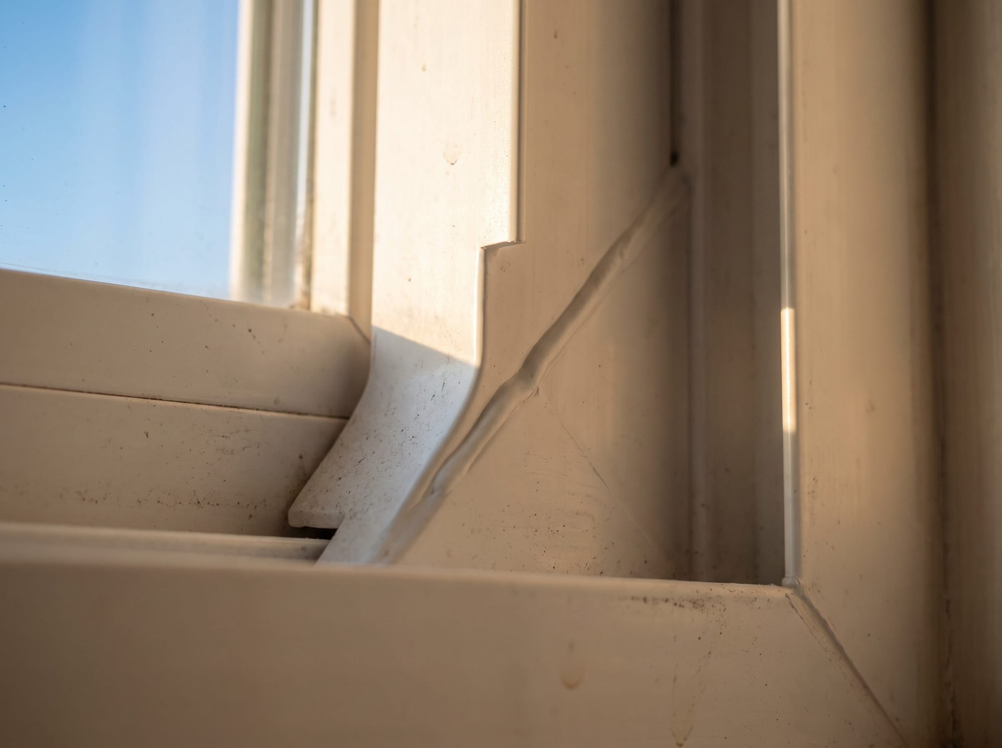 Macro of a premium white vinyl window frame corner that is fusion-welded into one continuous seamless piece with a faint smooth weld bead and no gap.