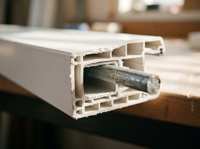 Cut cross-section of a premium white vinyl frame profile with a metal reinforcement stiffener filling the main structural chamber inside the vinyl walls.
