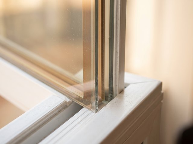 Macro of the edge of a premium insulated glass unit in a white vinyl sash — a warm-edge spacer and a faint low-emissivity coating giving the glass a slight tint and sheen.
